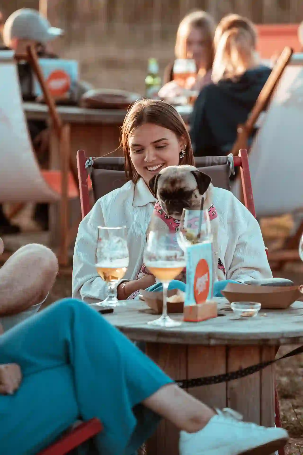 Een mopshond zit gezellig op schoot aan een tafeltje met wijn